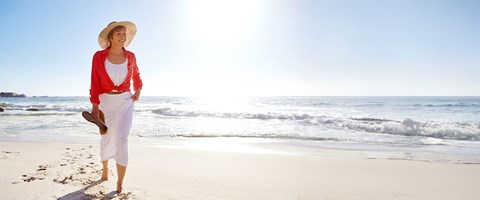 Moden dame med solhatt og kjole på stranden. 